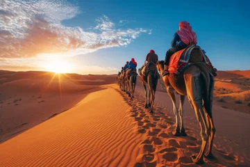 Schilderijen op glas A nomadic tribe traverses the expansive sahara, their arabian camels carrying them through the singing sands and over towering dunes, as the sun sets over the aeolian landscape © Pinklife