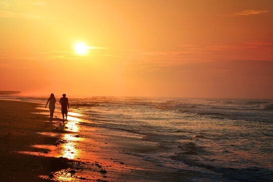 a silhouette of a young couple taking a walk along the beach at sunrise travel destination vacation