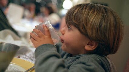 Closeup child drinking glass of water at restaurant. kid refreshing himself after meal, hydration...