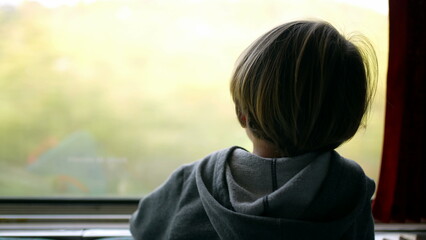Back of child traveling by train looking at scenery pass by while leaning on glass. Pensive Little...