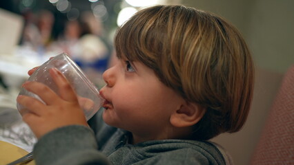 Closeup child drinking glass of water at restaurant. kid refreshing himself after meal, hydration concept