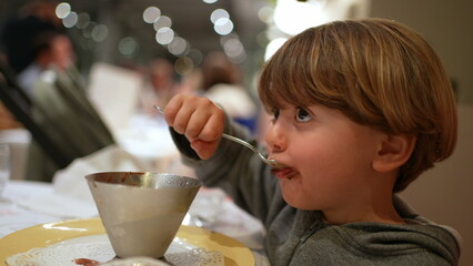 Child grabbing spoon and eating ice-cream dessert at restaurant, Small boy enjoying sugar food at...