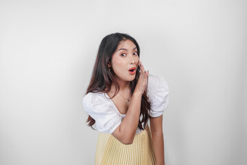 A young beautiful Asian woman is shouting and screaming loud with a hand on her mouth, isolated by white background.