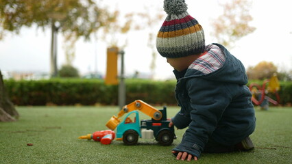 Little boy playing with truck outside at park during autumn day. Child wearing beanie and jacket...