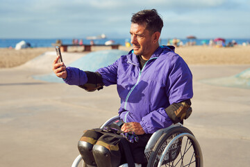 portrait disabled athlete man in wheelchair taking a selfie with a smartphone at skatepark