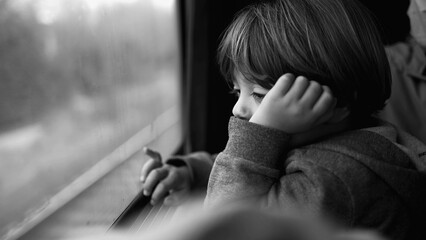 Little boy staring at landscape pass by from train seat in monochromatic. Black and white scene of child traveling and daydreaming