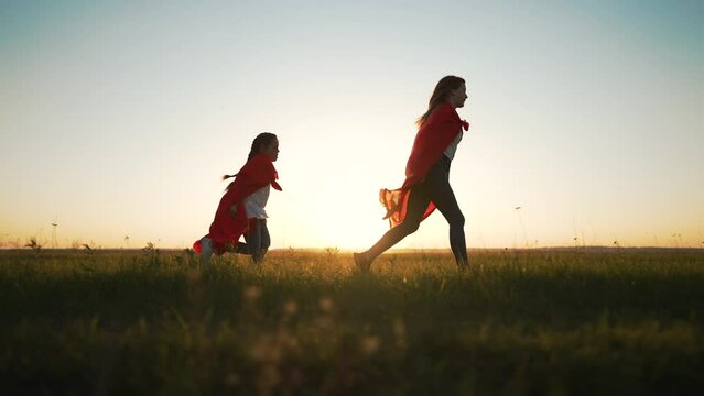 happy family. Child in superhero costume in park on green grass. Family dream in nature. Brave children run to success. Strong girls winners play superhero in park in summer. Red raincoats at sunset