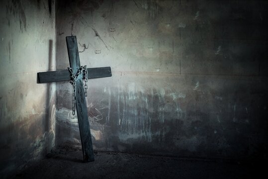 Black cross against wall with hanging steel chain and gun. Halloween day party festival celebration. Ancient sign of religion. Dark and scary tone
