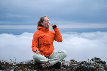 Hiker girl healthy outdoor lifestyle eating protein bar on mountain hiking, happy people eat healthy bar snack living active lifestyle in nature, travel,  tourism, sports concept