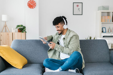 Young african american man using digital device relaxing on sofa at home. Millennial student boy holding digital device while sitting on couch
