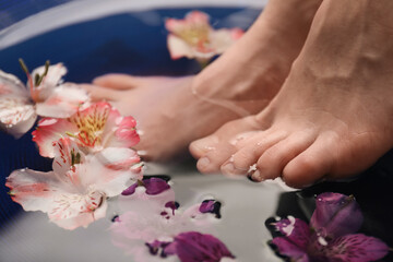 Obraz na płótnie Canvas Woman soaking her feet in bowl with water and flowers, closeup. Spa treatment