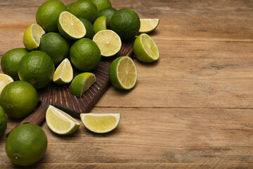 Fresh whole and cut limes on wooden table. Space for text