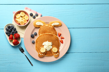 Fototapeta na wymiar Creative serving for kids. Plate with cute bunny made of pancakes, berries, cream and banana on light blue wooden table, flat lay. Space for text