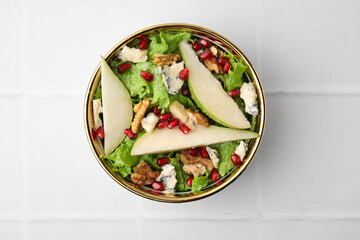 Delicious pear salad in bowl on light tiled table, top view