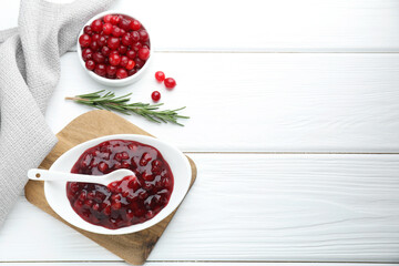 Tasty cranberry sauce in bowl, fresh berries and rosemary on white wooden table, flat lay. Space for text