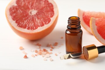 Grapefruit essential oil in bottle, pipette, sea salt and fruit on white table, closeup