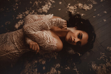 Mysterious Caucasian woman in white lace dress lying on a dark wooden floor surrounded by white...