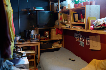 Corner of small apartment with kitchenware on wooden table standing next to shelf with old TV set,...