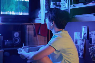 Young Asian woman with empty bowl and chopsticks sitting in front of old TV set and watching movie...