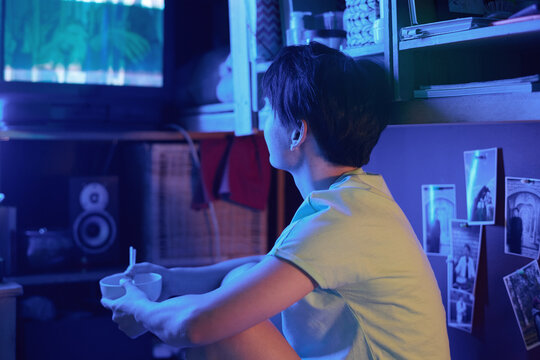 Young Asian Woman With Empty Bowl And Chopsticks Sitting In Front Of Old TV Set And Watching Movie Or Broadcast After Lunch At Home