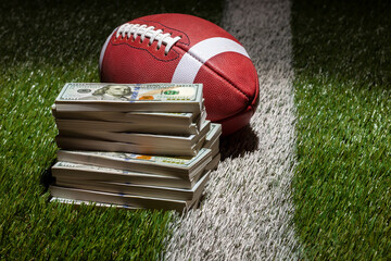 Football and a pile of one hundred dollar bills on a grass field with stripe and dark background