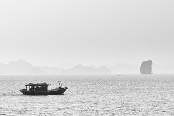 Fishing boat on a foggy day in Ha Long Bay with rock formation on the right