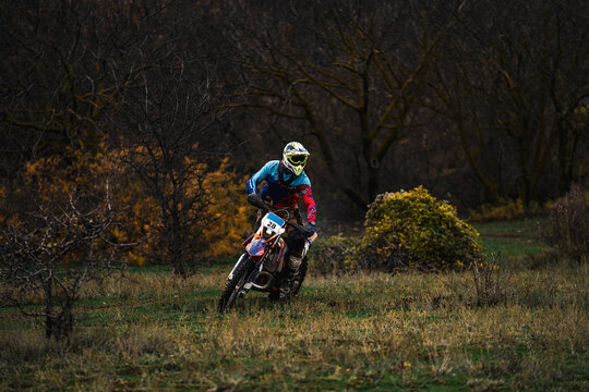 Professional motorcyclist in full moto equipment riding crops enduro bike through a green mountain meadow, motocross rider, concept of motosport, speed, hobby, journey, activity