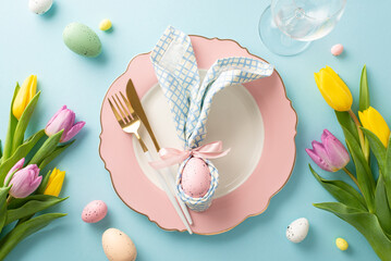 Bunny-themed Delight: Top-down view of an enchanting Easter table setting with bunny ear napkin, plate, cutlery, wine glass, tulips, and colorful eggs. Pastel blue background