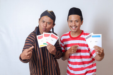 Portrait of two excited Indonesian man from Javanese and Madurese tribes holding voting paper for General Election (Pemilu) of president and government of Indonesia. Isolated image on gray background - obrazy, fototapety, plakaty