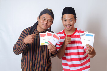 Portrait of two excited Indonesian man from Javanese and Madurese tribes holding voting paper for...