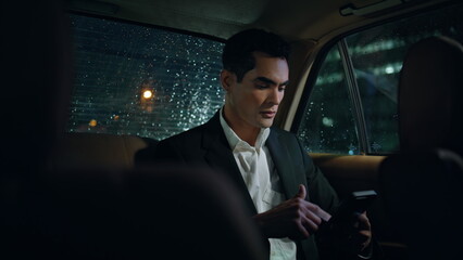Serious man scrolling phone in evening auto close up. Businessman working at car