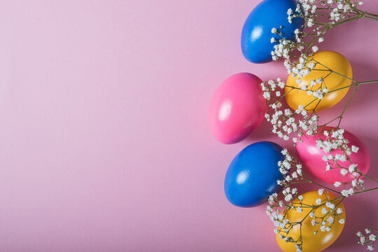 Colorful naturally dyed Easter eggs and spring flowers on pastel pink background, top view, flat lay style. Copy space for text.