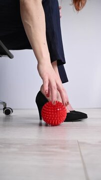 Business woman massages her feet on a massage ball with spikes. Vertical video. 