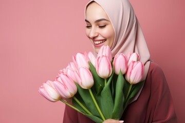 Cute beautiful young smiling Muslim girl in pink hijab with bouquet of tulips on pink background. Concept of spring, female beauty, March 8 holiday, international women's day, mother's day