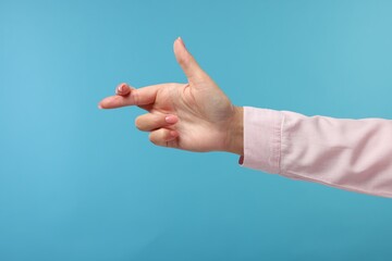 Woman crossing her fingers on light blue background, closeup