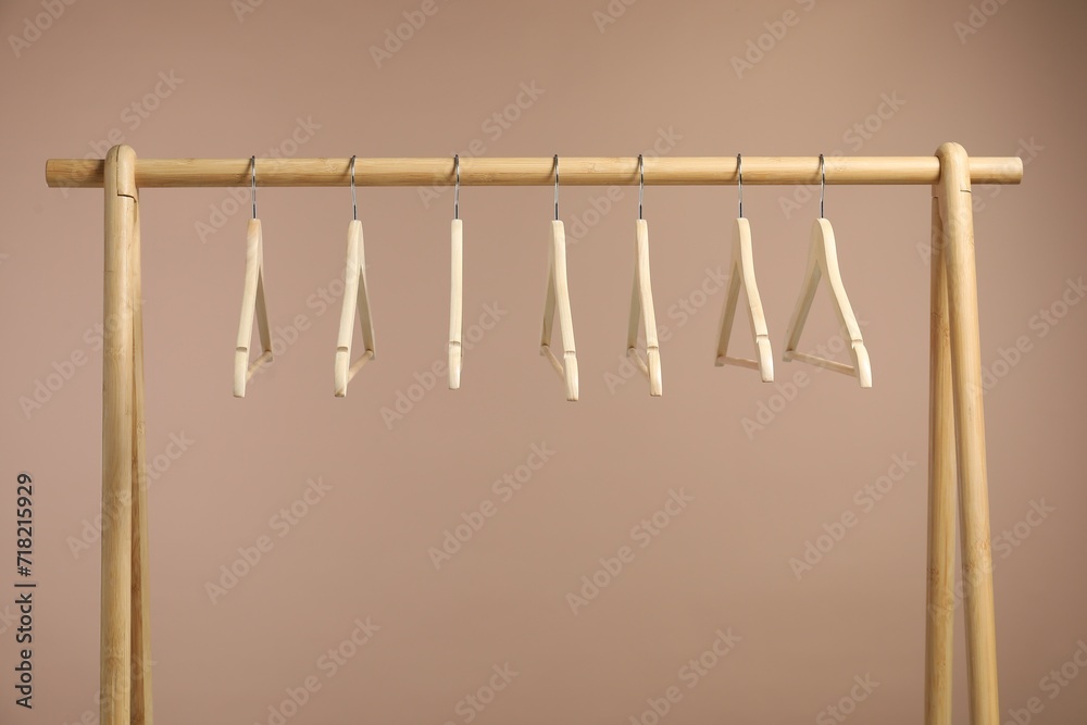 Poster Empty clothes hangers on wooden rack against light brown background