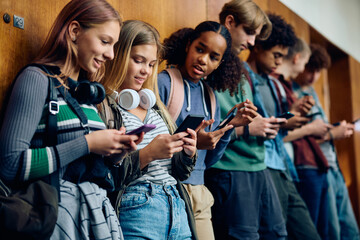 Multiracial group of high school students using their cell phones in hallway.
