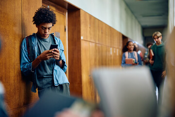Black high school student using smart phone in hallway.