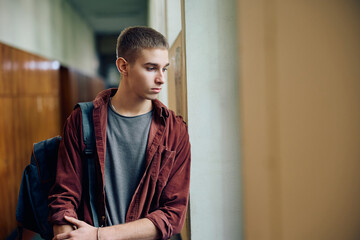 Thoughtful high school student looking through window in hallway.
