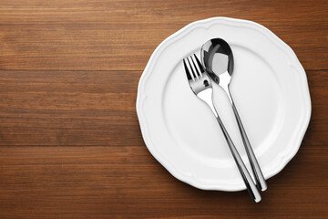 Clean plate, spoon and fork on wooden table, top view. Space for text