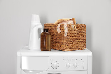 Baby clothes in wicker basket and laundry detergents on washing machine near light wall