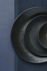 Stylish ceramic plates, bowl and napkin on dark blue background, top view