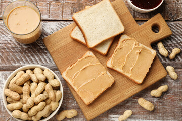 Tasty peanut butter sandwiches and peanuts on wooden table, flat lay
