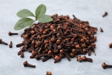 Pile of aromatic dried clove buds and leaves on grey table, closeup