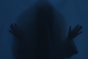 Silhouette of creepy ghost behind dark blue cloth