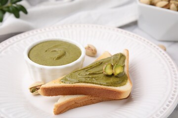 Tasty pistachio cream in bowl, nuts and toasts on white plate, closeup