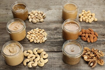 Tasty nut butters in jars and raw nuts on wooden table