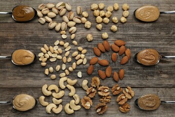 Tasty nut butters in spoons and raw nuts on wooden table, flat lay