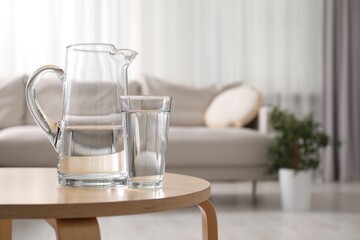 Jug and glass with clear water on wooden table indoors. Space for text