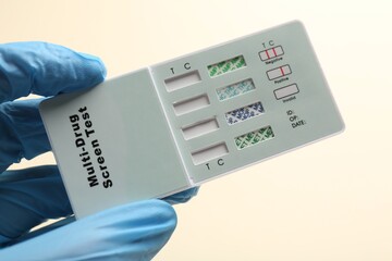 Doctor holding multi-drug screen test on beige background, closeup